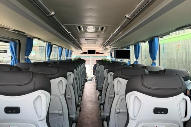 Inside a bus with grey and white cushioned seats along the aisle