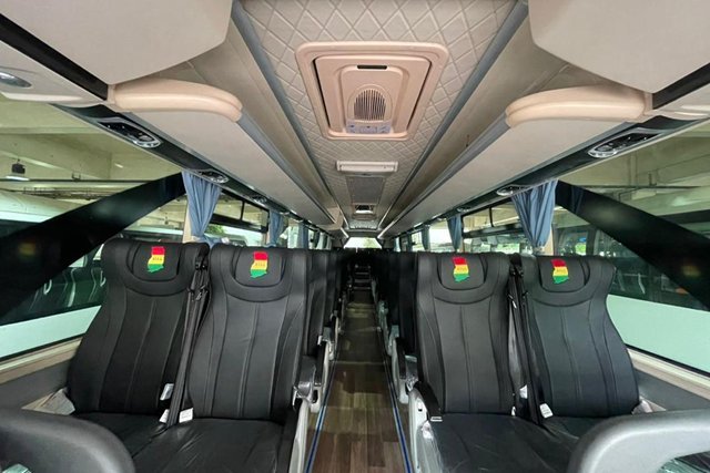 Inside a bus: rows of cushioned seats with Ghana flag headrest covers marked B.T.L.L.